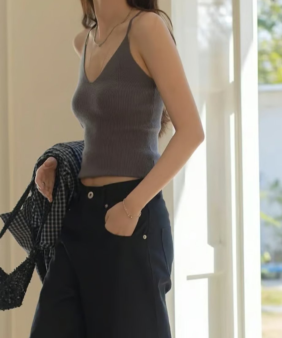 チャコールグレーのリブ編みVネックキャミソールを着用した女性の半身。黒のチェック柄シャツを手に持ち、黒のボトムスを着用。