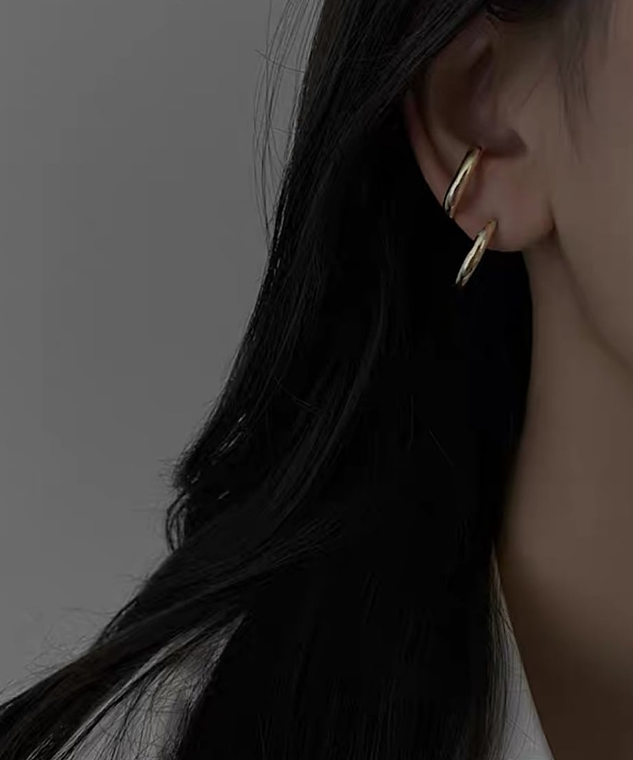 耳元で緩やかな曲線を描くゴールドの変形フープピアスを着用した女性.。
