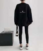 黒のオーバーサイズスウェットを着用した女性の後ろからの全身ショット。黒スキニーとスニーカーをコーディネートしている。