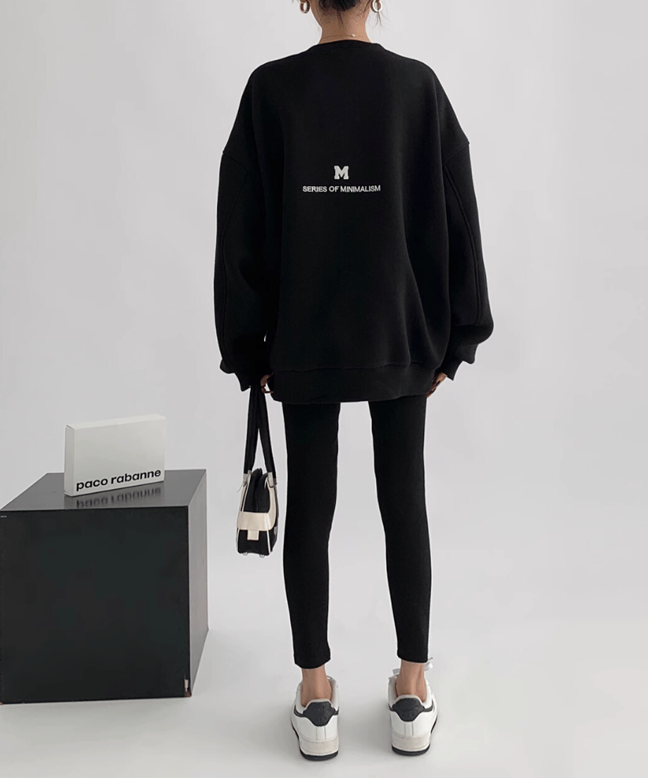 黒のオーバーサイズスウェットを着用した女性の後ろからの全身ショット。黒スキニーとスニーカーをコーディネートしている。