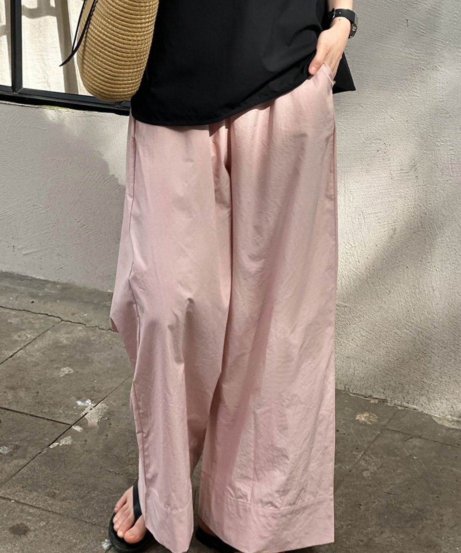 ピンクのワイドレッグパンツを着用し、黒のトップスを合わせた女性の、屋外の壁を背景にした下半身サイドビュー