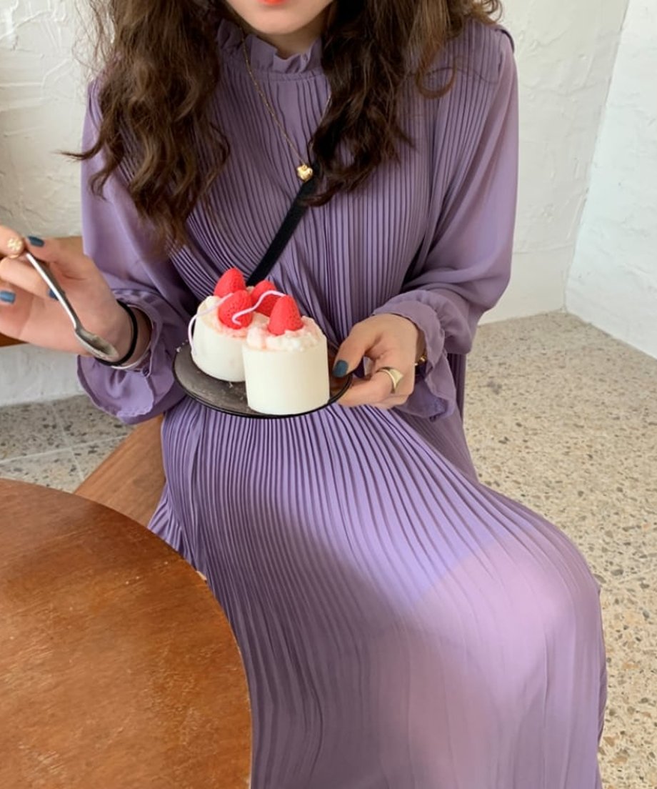 カフェで椅子に座り、プリーツが美しく広がるパープルワンピースを着用してスイーツを楽しむ様子