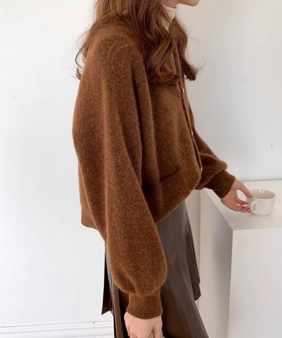 コーヒーのランタンスリーブショートカーディガンを着用し、濃い茶色のスカートを合わせた女性の横向きのバストアップ。ふんわりとした袖のボリューム感が特徴。