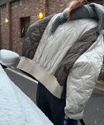 シルバーグレーのツートンキルトジャケットを着用し、雪が積もった車に寄りかかる女性の背面。グレーのマフラーとリブ仕様の裾。