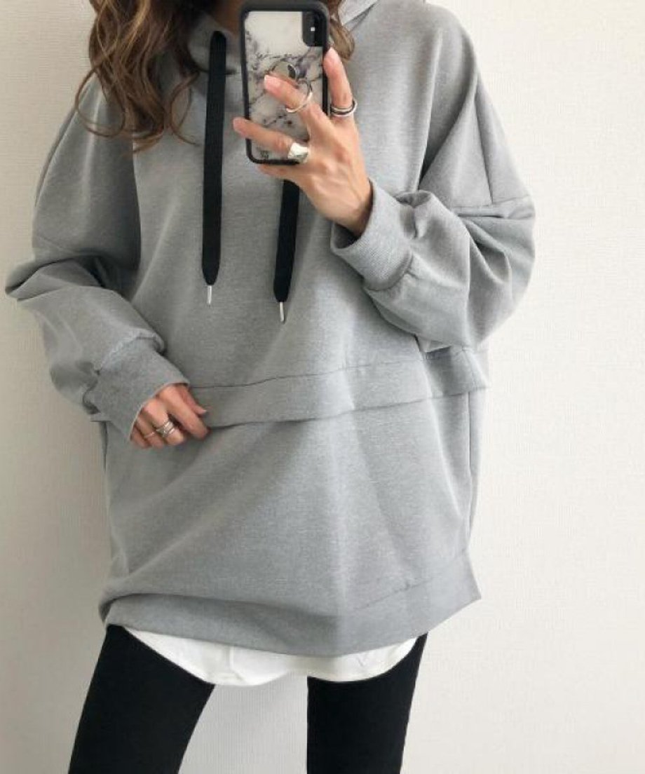 グレーのフーディーを着用し、黒のスキニーパンツと黒のロングブーツを合わせた女性の腰から下の立ち姿
