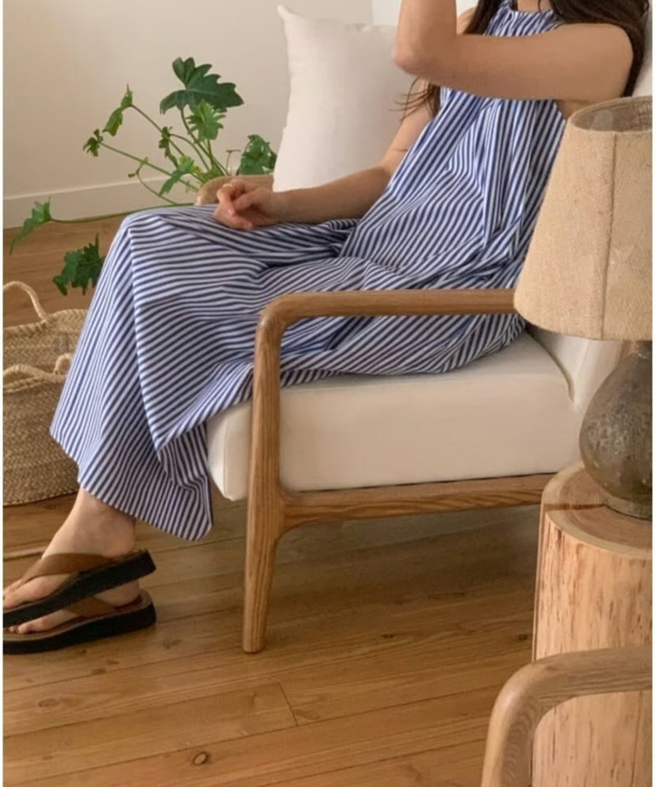 ストライプワンピースを着用して白いソファに座る女性の足元とサイドシルエット。