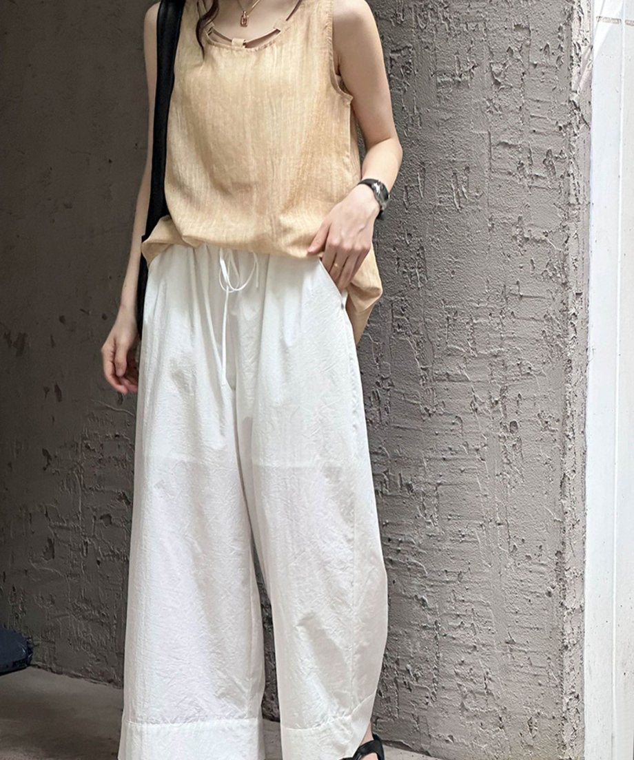 白いワイドレッグパンツを着用し、ベージュのノースリーブトップスを合わせた女性の、屋内の全身写真
