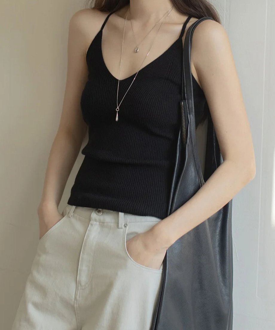 黒のリブ編みVネックキャミソールを着用した女性の半身。ライトベージュのパンツとシルバーのネックレスを着用。