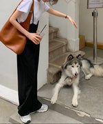 ブラックのハイウエストサスペンダーパンツを着用し、階段に座る犬に手を差し伸べる女性。