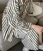 ソファに座り、サイドから見たストライプセットアップのシルエットと柔らかな生地の重なり。