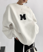 白いオーバーサイズスウェット。「M」ロゴプリントが施されている。