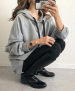 グレーのオーバーサイズフーディーを着用した女性が、黒のスキニーパンツとロングブーツを合わせ、座っている全身ショッ