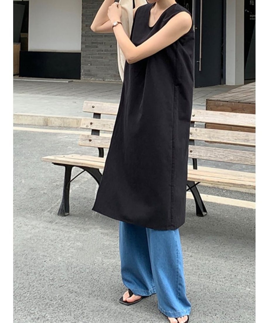 ブラックチュニックを規定る女性。サイドスリットから覗くパンツと、手に持ったバック。