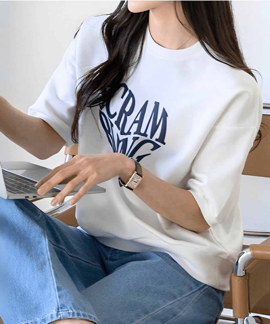 白いTシャツを着た女性が椅子に座り、ノートパソコンを操作している様子。