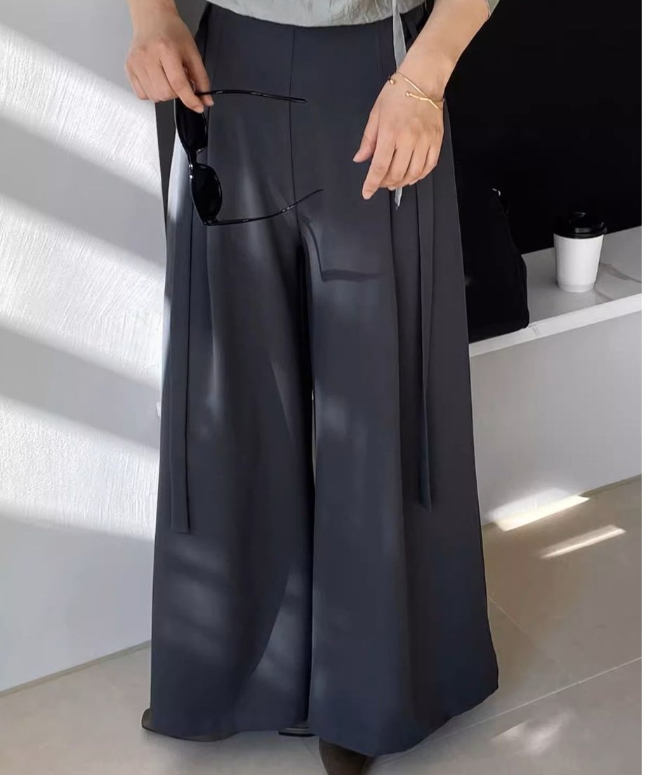 グレートップスと合わせたブラックのワイドレッグプリーツパンツ。手にサングラスを持つ。