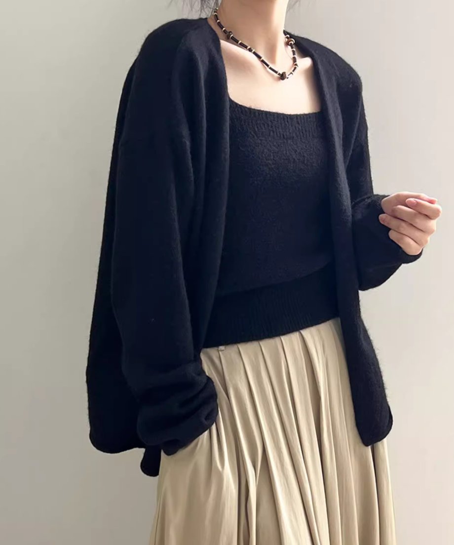 ブラックのニットキャミソールアンサンブルをセットで着用した女性の半身像。カーディガンは袖をまくり、ベージュのプリーツロングスカートを着用。