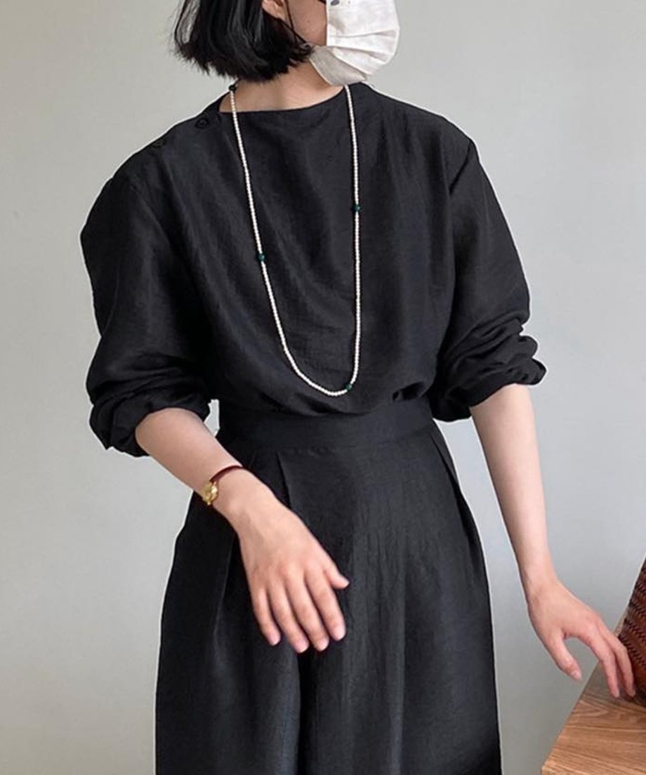 ブラックのセットアップを着用し、ロングネックレスを合わせた女性。