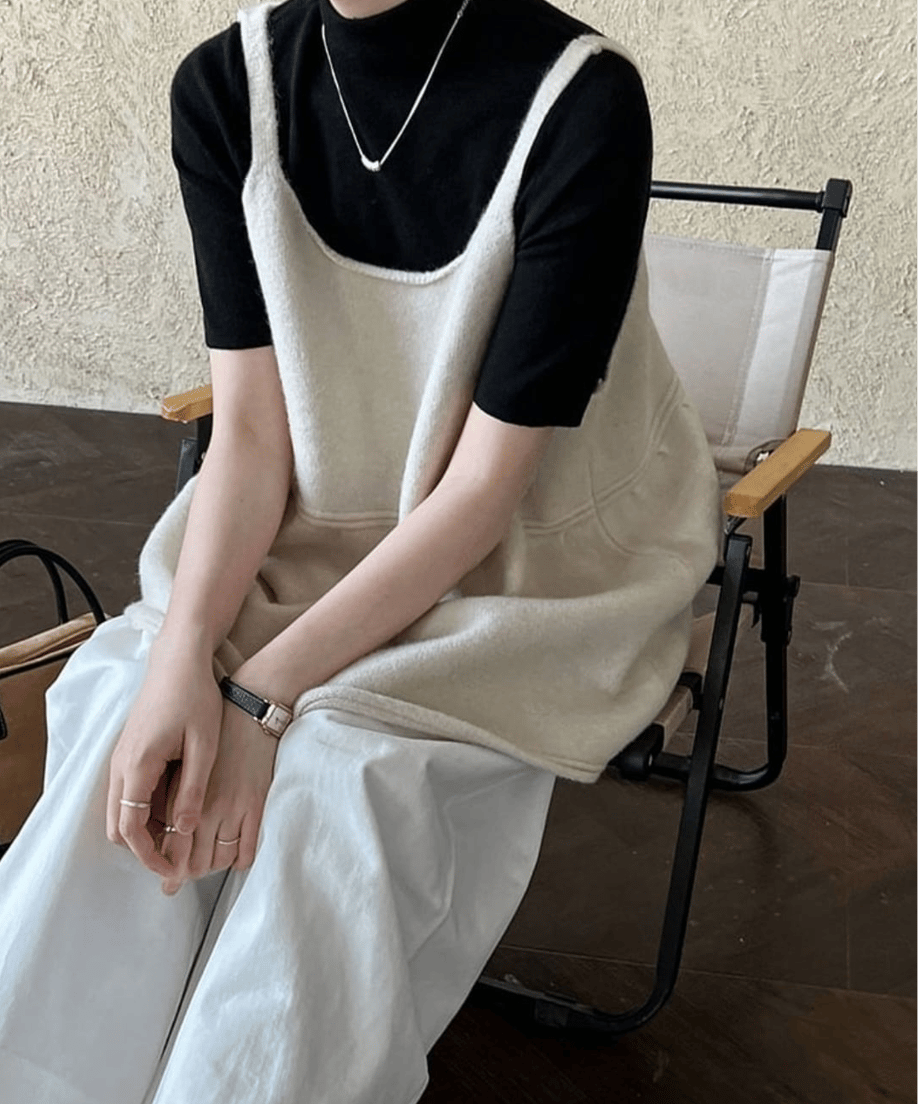 オフホワイトのチュニックにホワイトのパンツをコーディネートして椅子に座っている写真