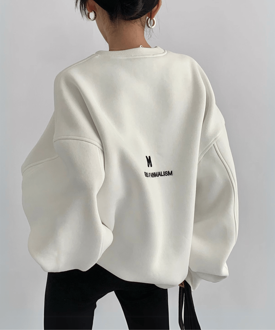 白いオーバーサイズスウェットの背中側。小さな「M」ロゴと「SERIES OF MINIMALISM」の英文プリントが施されている。