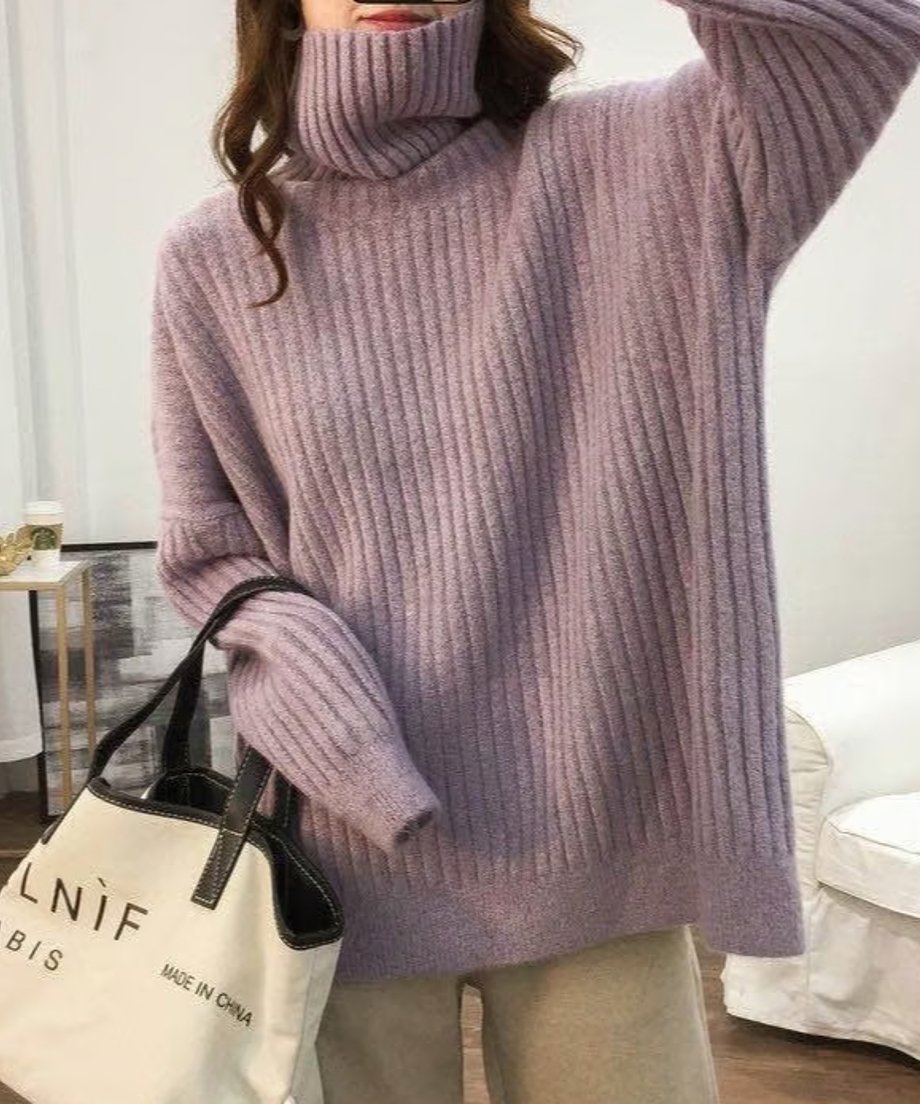 パープルのオーバーサイズタートルネックニットを着用し、ロゴ入りの白いトートバッグを持っている女性の上半身。