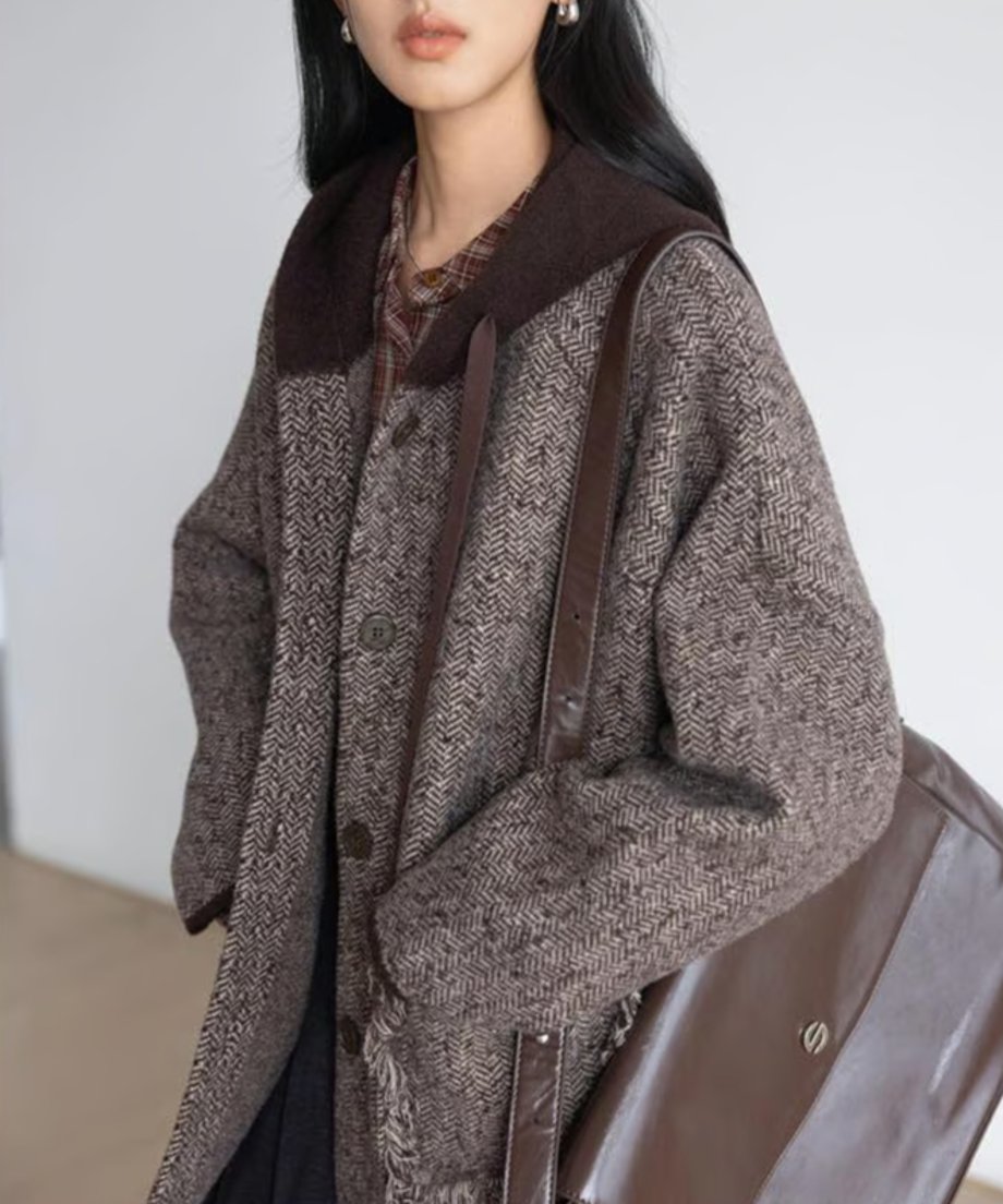 フリンジフード付きジャケットを着用し、茶色のショルダーバッグを肩にかけた女性のバストアップ。ポケット口のフリンジと、チェック柄のインナーシャツが見える。