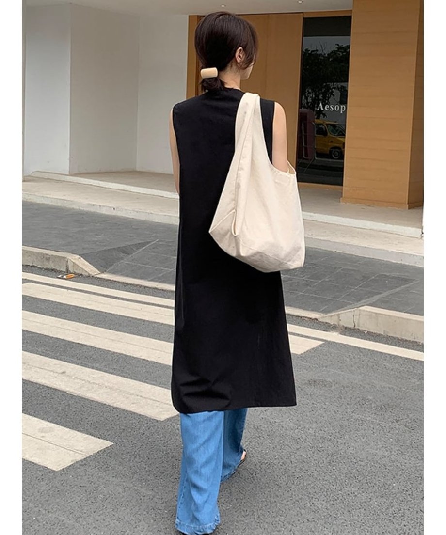 黒のノースリーブチュニックとブルーデニムを合わせた、後ろ姿の女性。背の高い建物と横断歩道がある屋外。