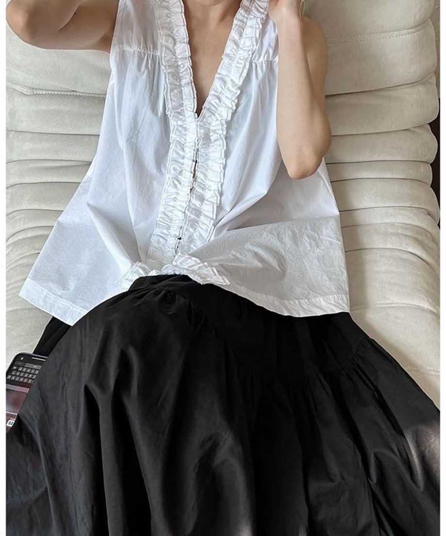 白のノースリーブチュニックブラウスと黒のロングスカートを着用した女性が白いソファーに座った写真。