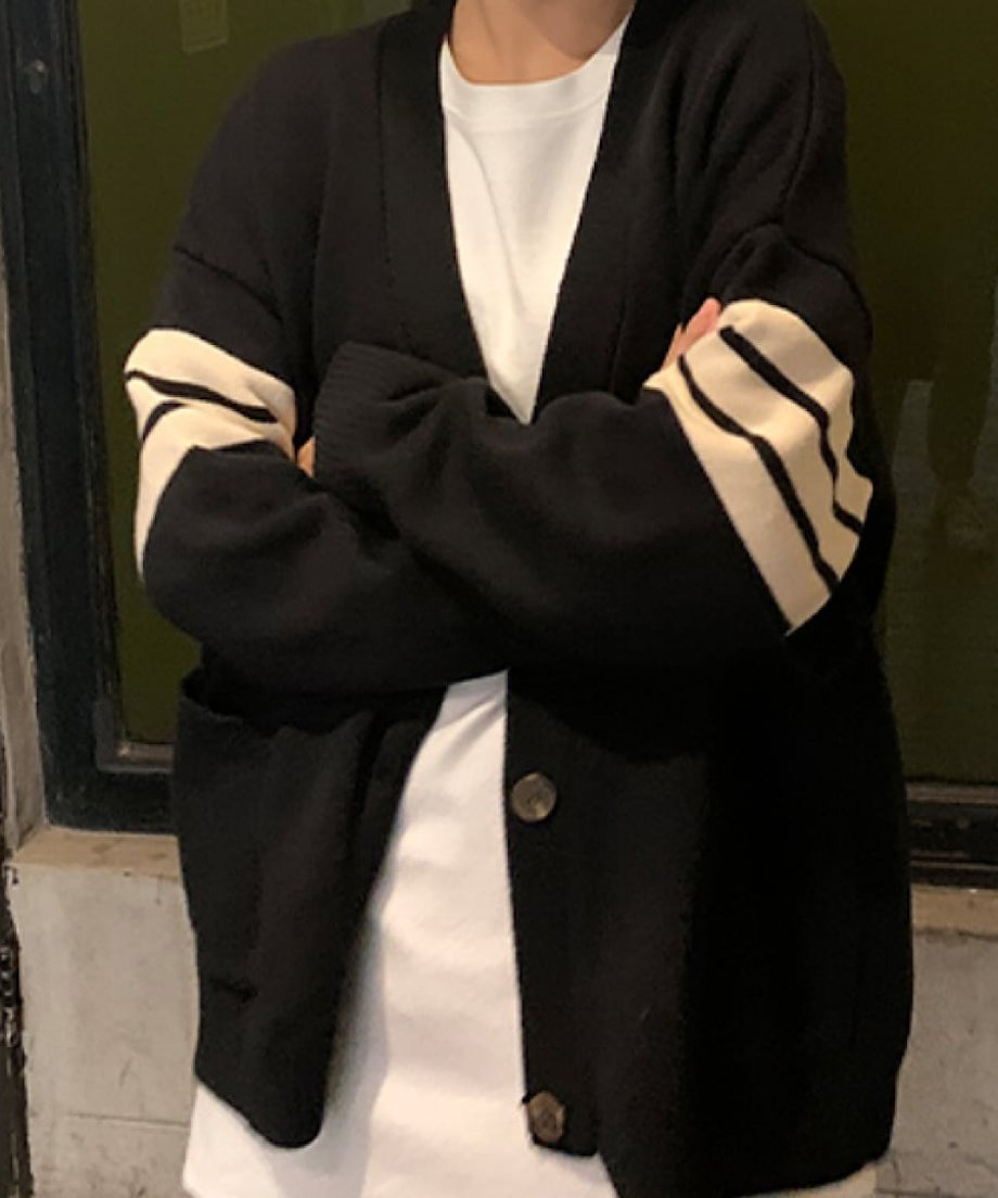 黒いライン入りオーバーサイズカーディガンを白いTシャツの上に着て、腕を組んでポーズをとる写真。