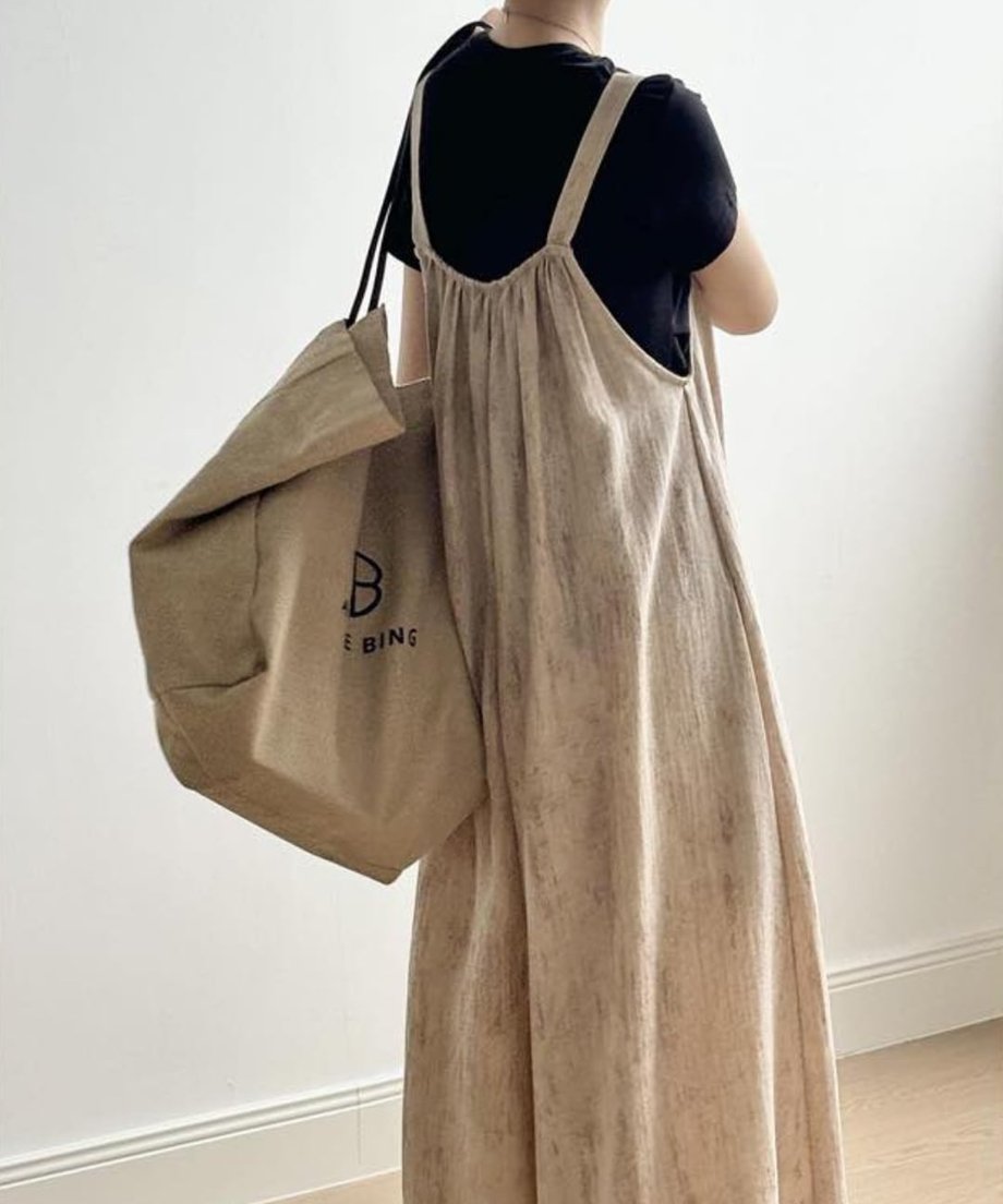 ベージュのワイドオーバーオールを後ろから撮影した写真。黒Tシャツをインナーに、ベージュのキャンバストートバッグを肩にかけている。