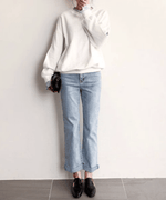 ホワイトのレイヤードスウェットを着用した女性の全身画像。フリルネックと袖口からブルーストライプの生地が覗く重ね着風デザイン。薄いブルーのフレアデニムと黒のローファーを着用。