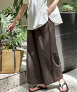 ブラウンのワイドレッグパンツと白いトップス、黒のビーチサンダルを合わせた女性の下半身側面。手にはカゴバッグを持つ。