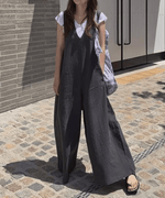 グレーのワイドレッグサロペットを着た女性が、白Tシャツをインナーに着用し、柄物の大きなバッグを肩にかけ、サンダルを履いて石畳の上で全身ショット。