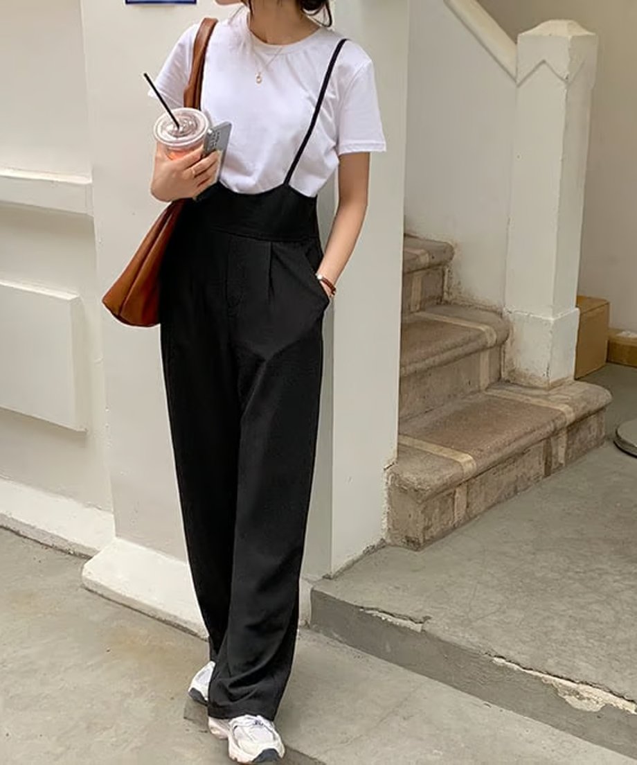 ブラックのハイウエストサスペンダーパンツと白Tシャツ、スニーカーを合わせたカジュアルな装いの女性。