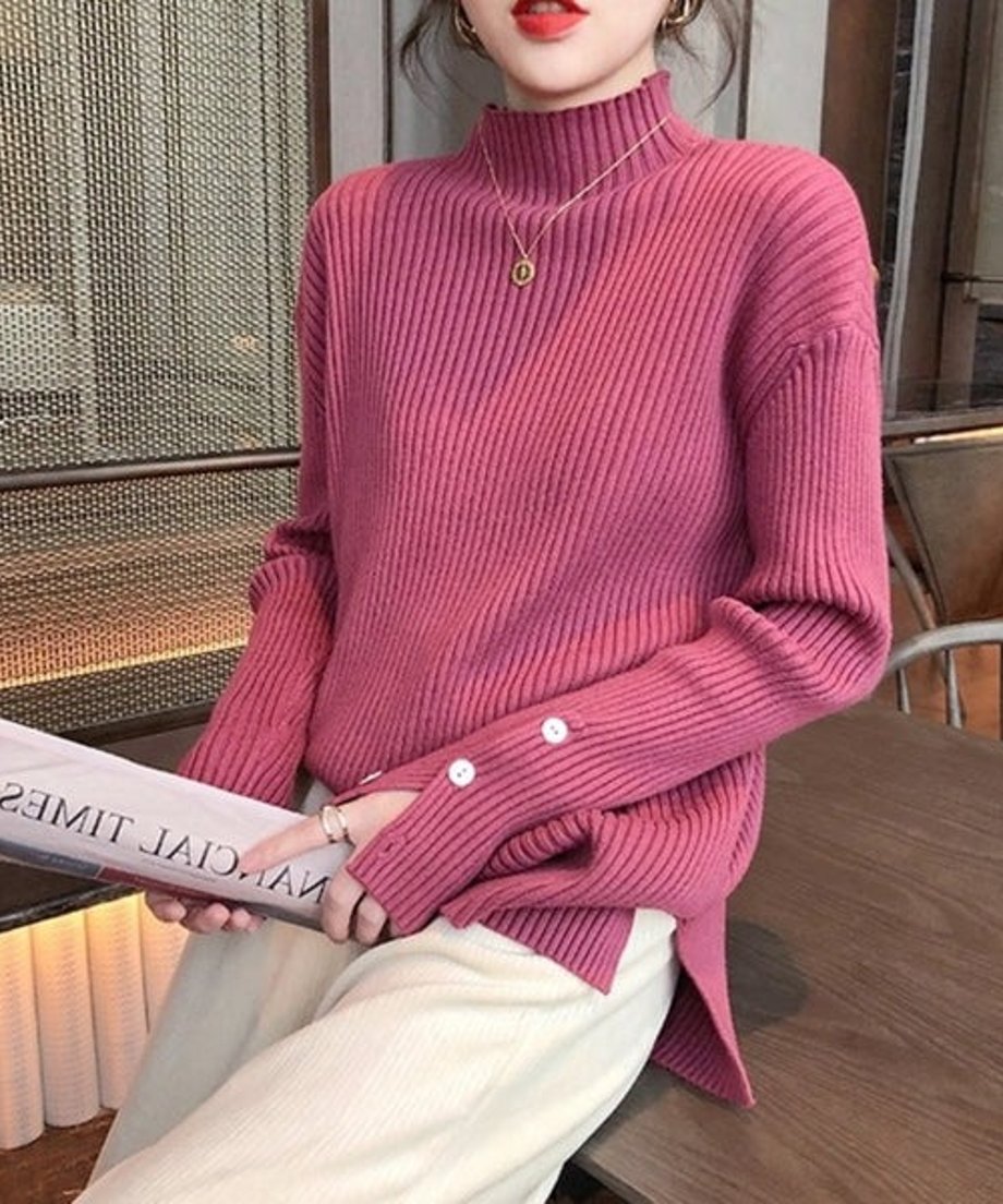 マゼンタのモックネックニットを着用し、白いパンツに裾をインした女性の上半身写真。袖口の白いボタンが3つ見える。