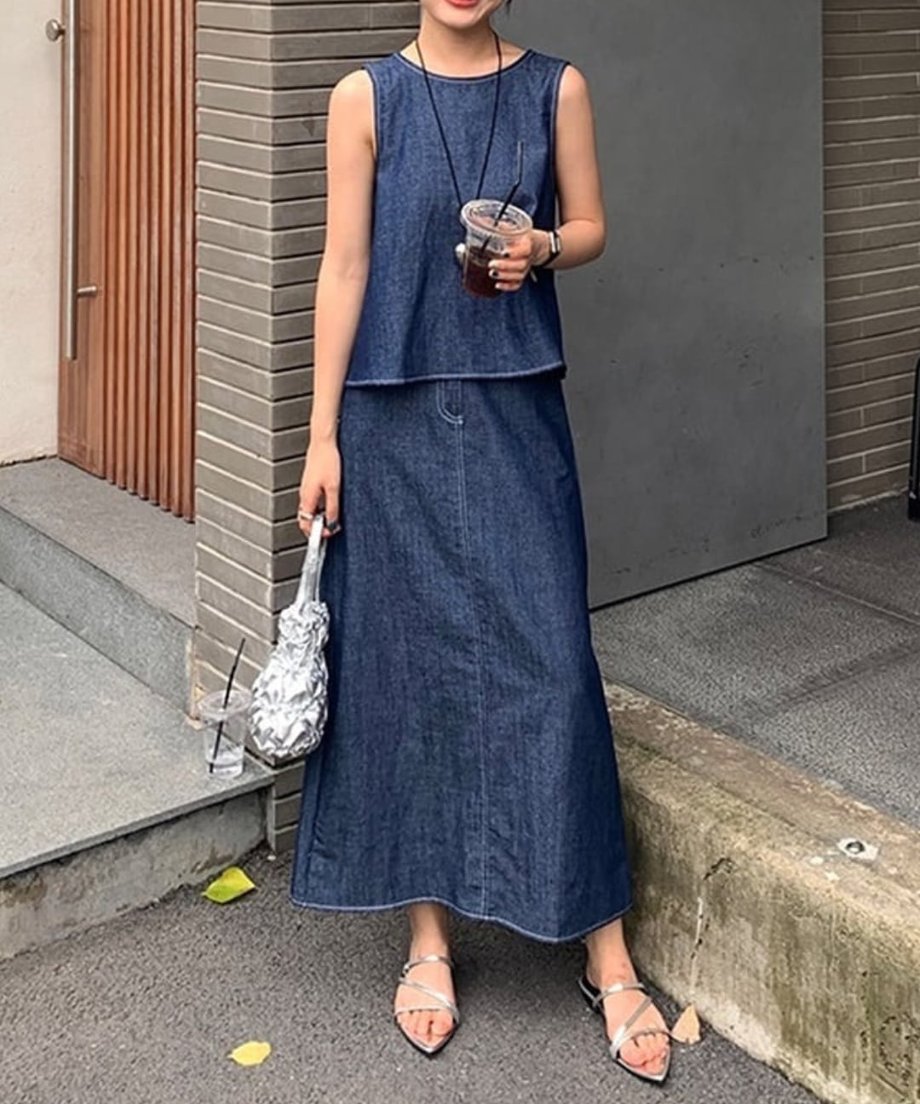 カフェの入り口で、ドリンクとシルバーバッグを合わせたデニムスリーブレスセットアップのデイリースタイル。