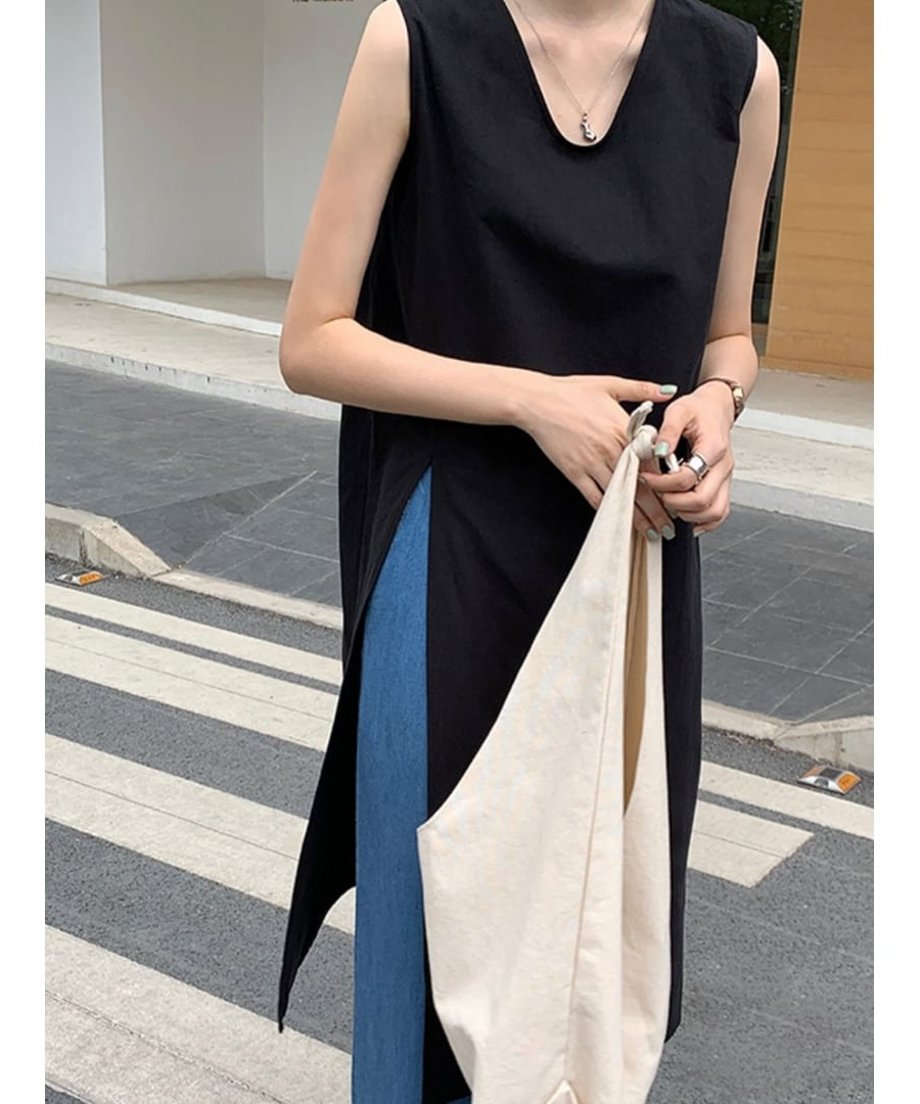 黒のサイドスリットチュニックにデニムを合わせ、白いキャンバストートバッグを持つ女性の手元。