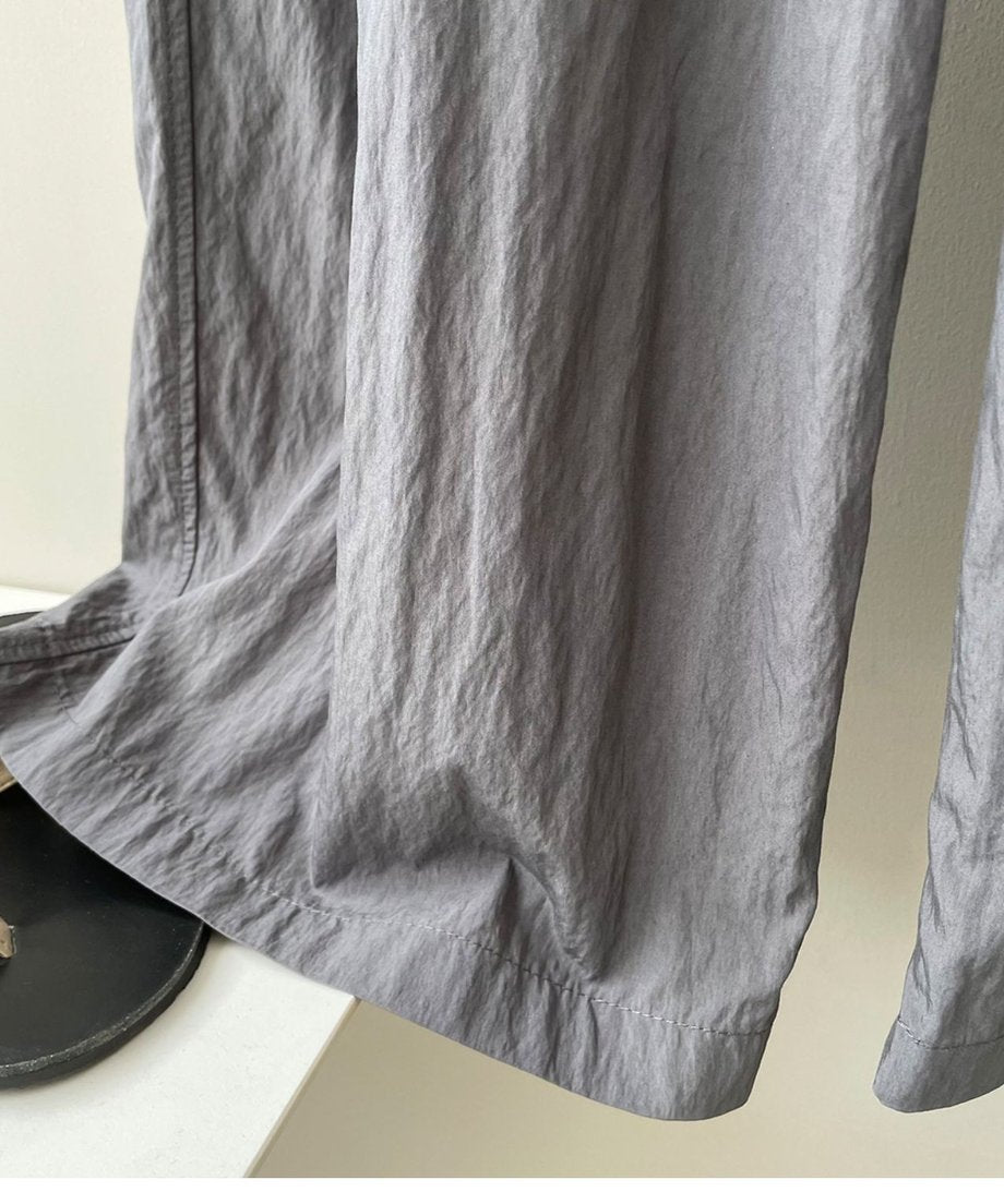 グレーのプリーツワイドパンツの裾と、黒いソールのサンダルが写っているクローズアップ。パンツの細かなシワ加工の質感がわかる。
