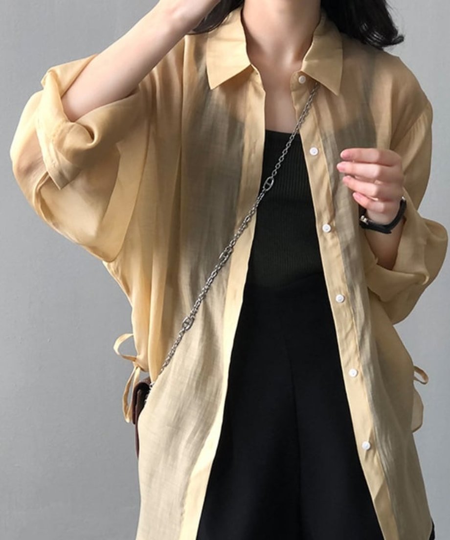 イエローオークのシアーシャツを着用し、袖を捲りあげた女性。