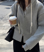 グレーのダブルジップデザインフーディを着用し、コーヒーカップを持つ女性の胸から下のコーディネート。黒のスカートと白のインナーを合わせたカジュアルな着こなし。