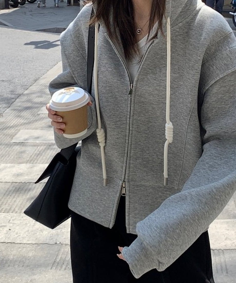 グレーのダブルジップデザインフーディを着用し、コーヒーカップを持つ女性の胸から下のコーディネート。黒のスカートと白のインナーを合わせたカジュアルな着こなし。