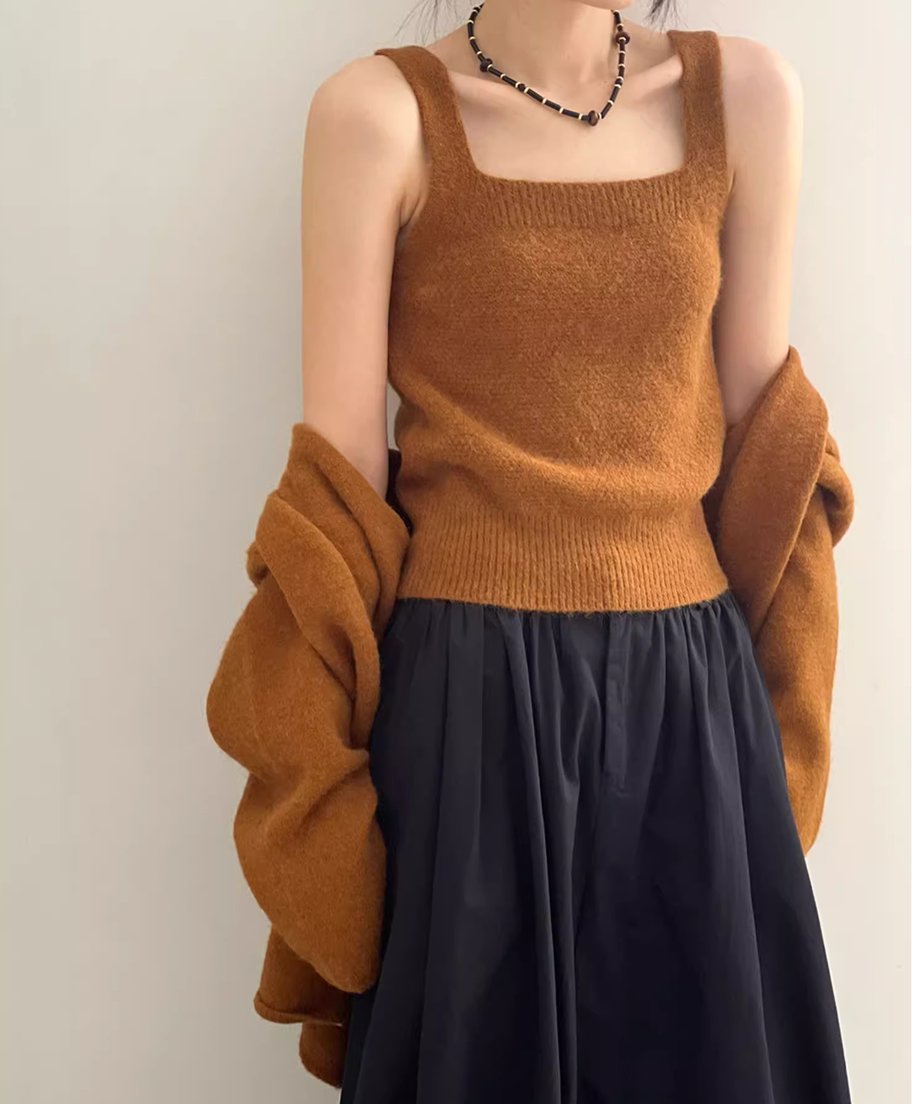 キャメルのニットキャミソールを着用し、カーディガンを肩にかけた女性の半身像。キャミソールはスクエアネックで、黒いロングスカートと太めのネックレスを着用。