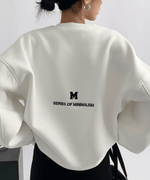 白いオーバーサイズスウェットの背中側。小さな「M」ロゴと「SERIES OF MINIMALISM」の英文プリントが施されている。
