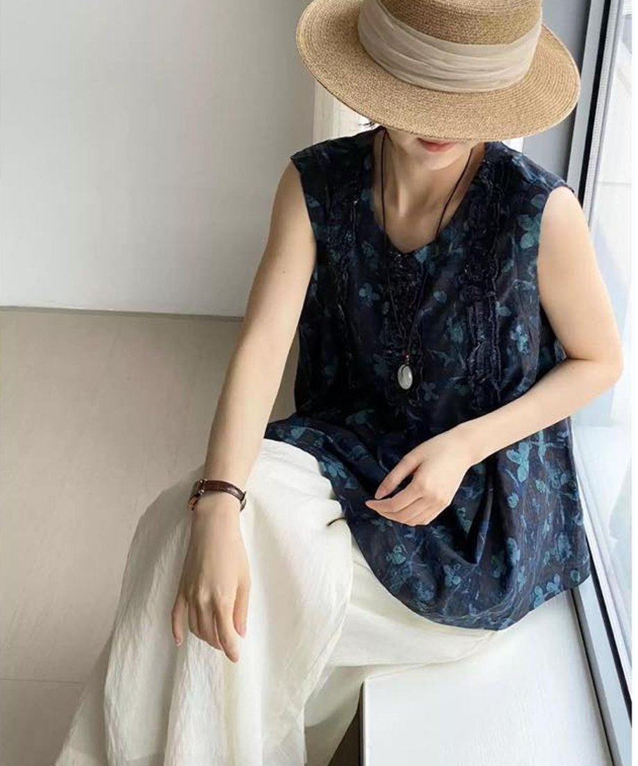 女性がネイビー花柄ブラウスと白パンツを着用し、帽子をかぶって座っている写真