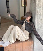 コンクリートの柱にもたれかかり座っている女性。ベージュのバギーワイドオーバーオールとボーダーシアーTシャツのコーディネートに、茶色のキャップと白いスニーカーを合わせている。
