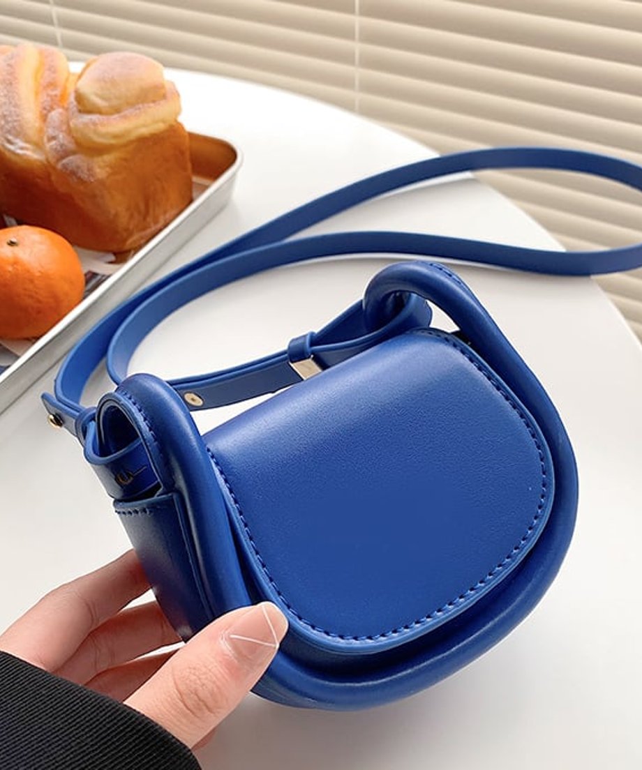 白いテーブルに置かれた鮮やかなブルーのミニバッグとパンのライフスタイルカット。