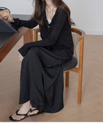 ブラックのドロストマキシスカートと黒のカーディガンを着用し、椅子に座っている女性の全身。スカートのドローストリングが正面に見える。