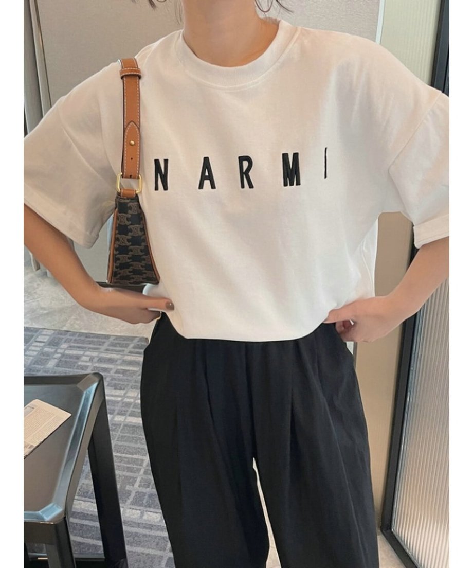 ホワイトのTシャツを両手でウエストに当て、ゆったりとしたサイズ感とシルエットを見せるモデル。