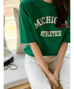 カフェで座っているグリーンのロゴTシャツを着た女性。