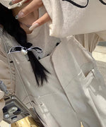 ベージュのオーバーオールと、長袖Tシャツの組み合わせ女性の上半身の接写。Tシャツの胸元のロゴと袖のハート柄が確認できる。スマートフォンを持っている。