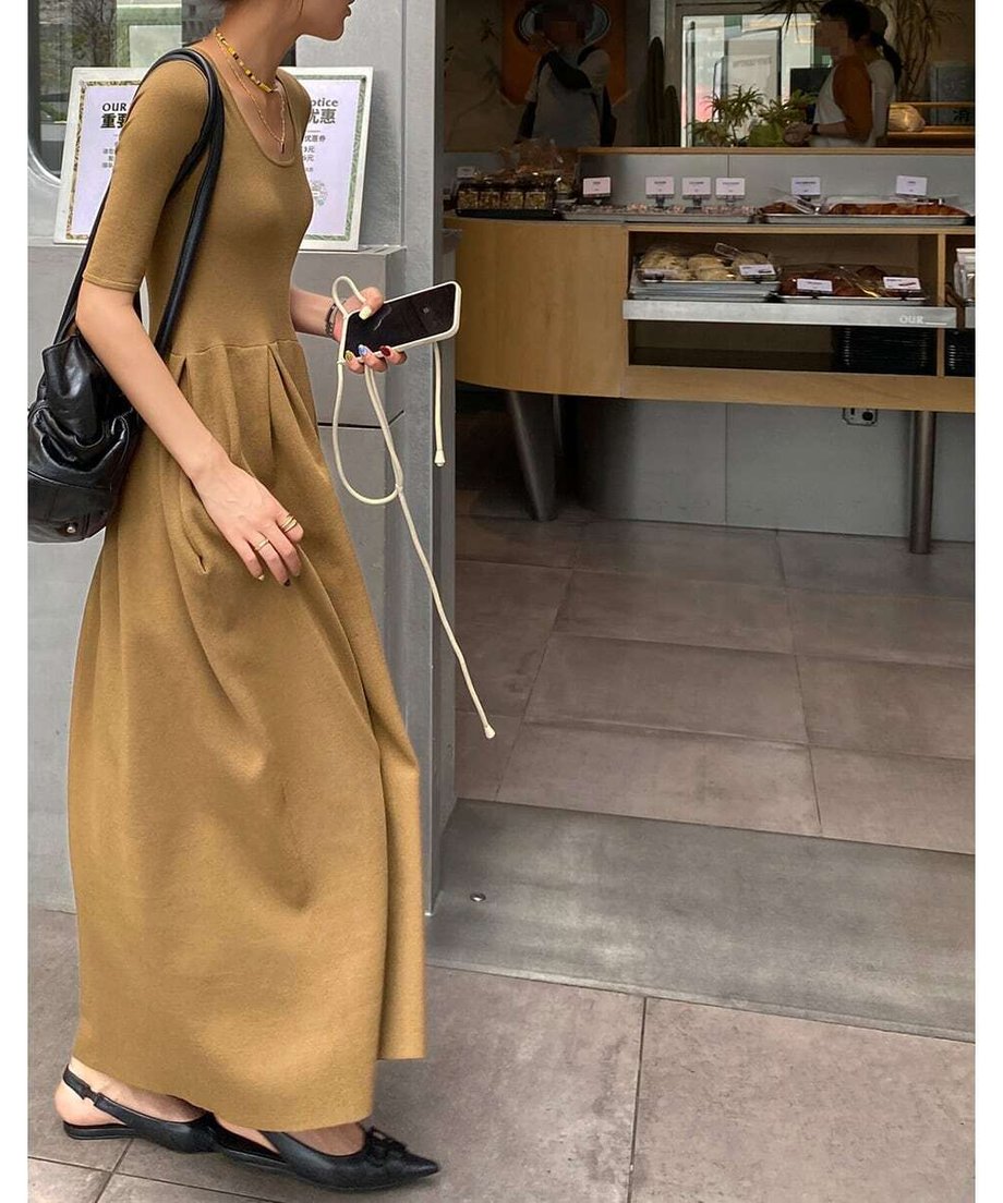 キャメルのウエストギャザーワンピースを着用した女性が、黒のバッグを肩にかけ店外を歩いている全身カット。